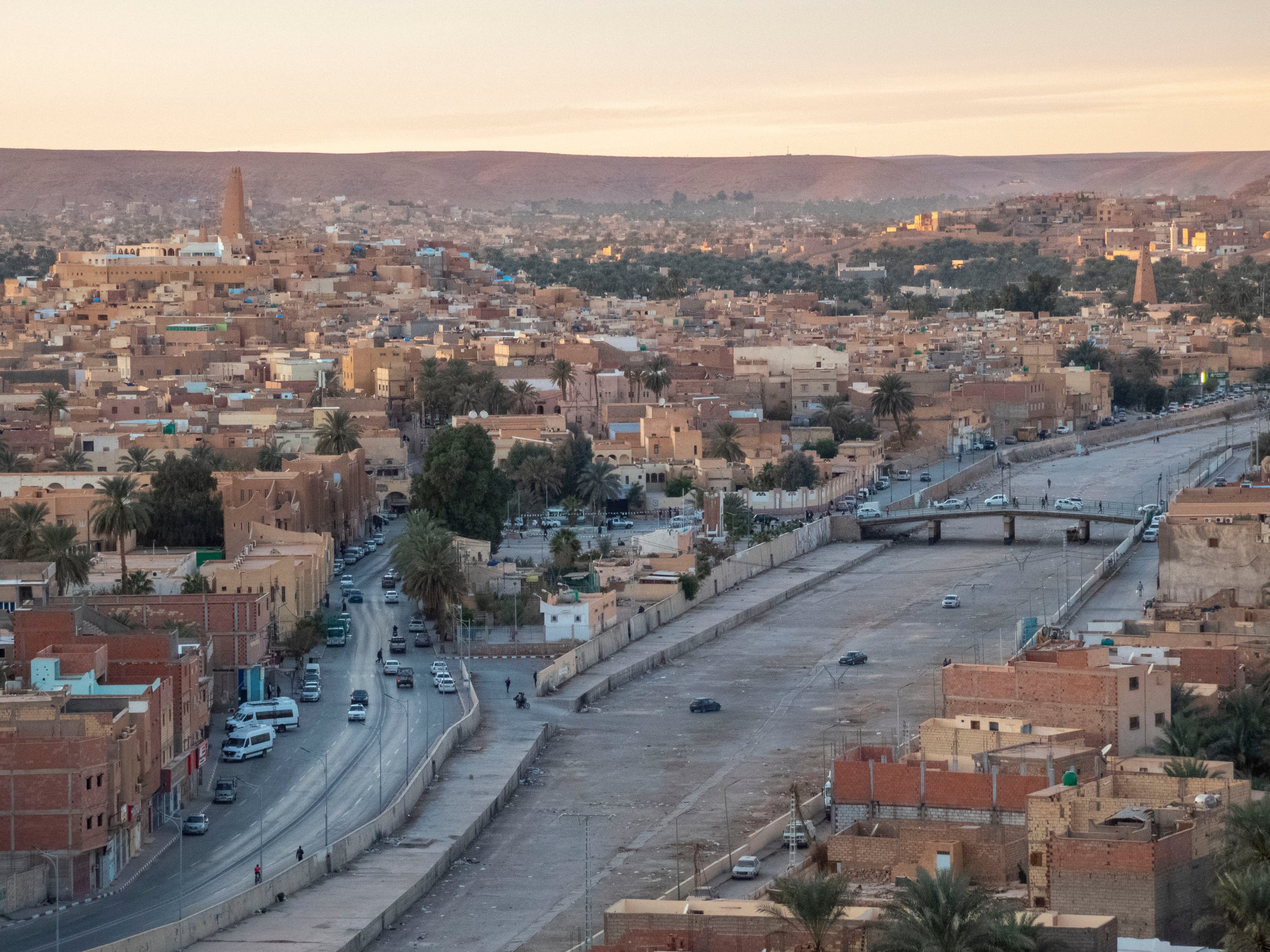 Vue de Ghardaïa depuis Melika : le ksar aux maisons ocre, la palmeraie et le lit asséché de l'oued M'zab, minaret au loin, lumière de fin de journée